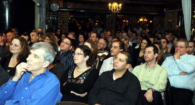 המשתתפים מאזינים דרוכים שנייה לפני פרץ צחוק נוסף. מי הצחיק אותם? עברו הלאה